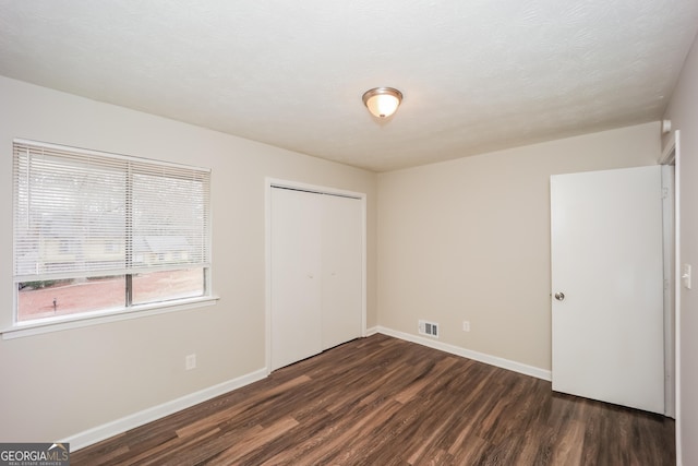 unfurnished bedroom with dark wood-type flooring and a closet