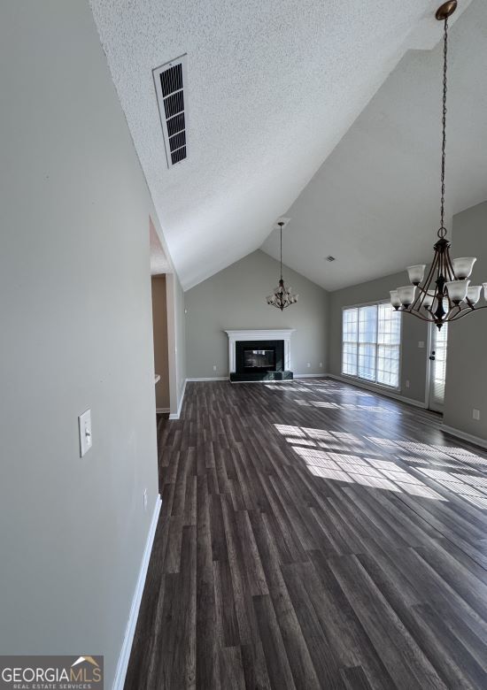 unfurnished living room with an inviting chandelier, dark wood-type flooring, lofted ceiling, and a textured ceiling