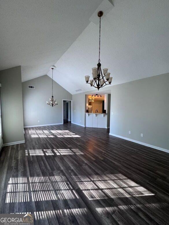 unfurnished living room featuring lofted ceiling, dark hardwood / wood-style floors, and a chandelier