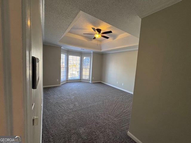 empty room featuring crown molding, a textured ceiling, a tray ceiling, dark carpet, and ceiling fan