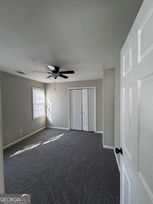 unfurnished bedroom with ceiling fan, dark carpet, and a closet