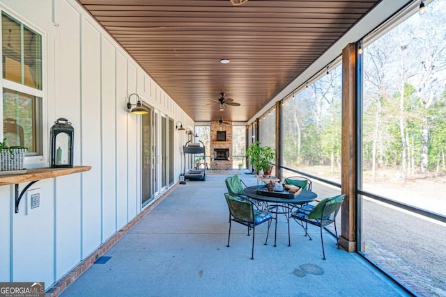 sunroom / solarium featuring ceiling fan, an outdoor stone fireplace, and wooden ceiling