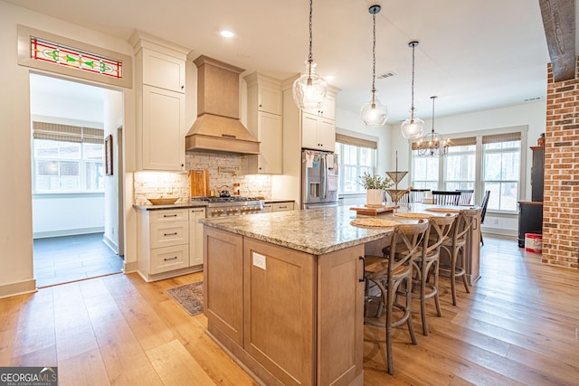 kitchen featuring premium range hood, pendant lighting, light stone counters, stainless steel appliances, and a spacious island