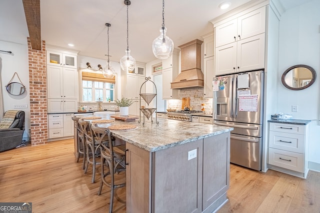 kitchen with white cabinets, a kitchen bar, custom exhaust hood, a kitchen island with sink, and stainless steel refrigerator with ice dispenser