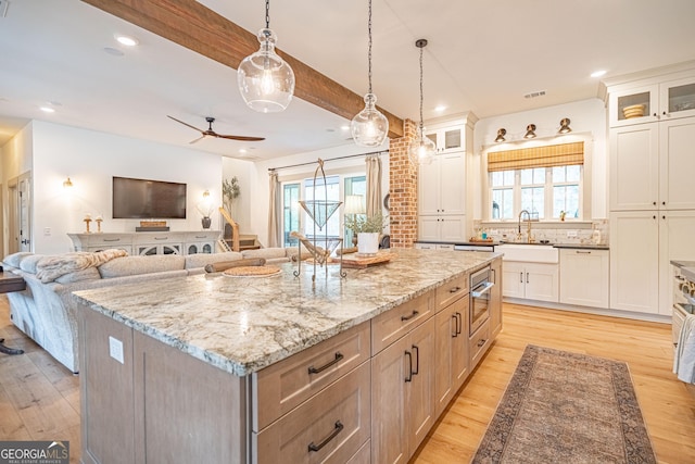 kitchen featuring a spacious island, sink, decorative light fixtures, light hardwood / wood-style flooring, and white cabinets