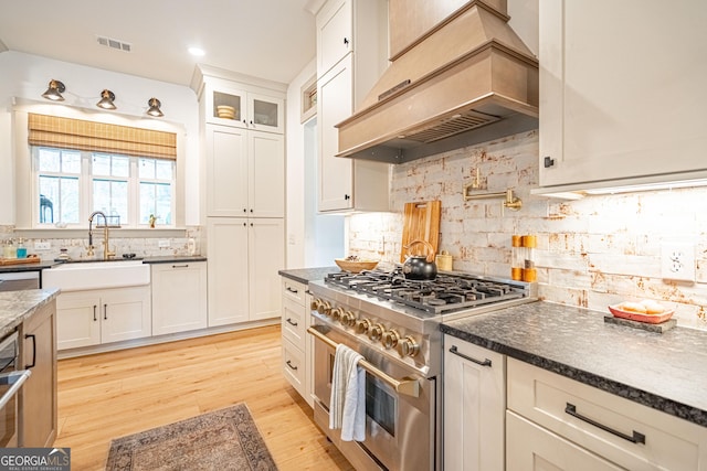 kitchen featuring white cabinetry, sink, custom exhaust hood, high end stainless steel range, and light hardwood / wood-style flooring