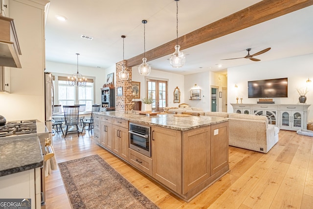 kitchen with appliances with stainless steel finishes, a spacious island, decorative light fixtures, dark stone counters, and light brown cabinets