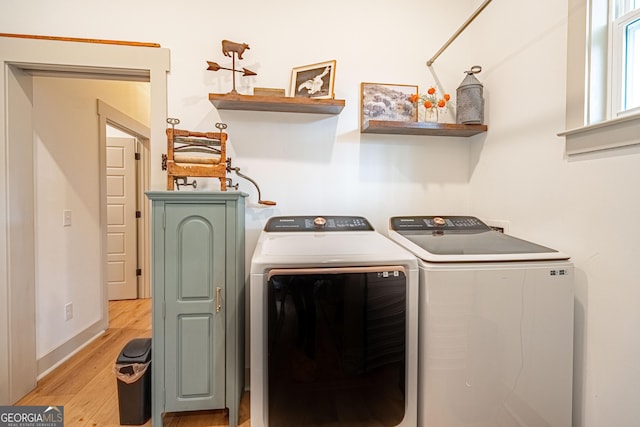 clothes washing area with washing machine and clothes dryer and light wood-type flooring