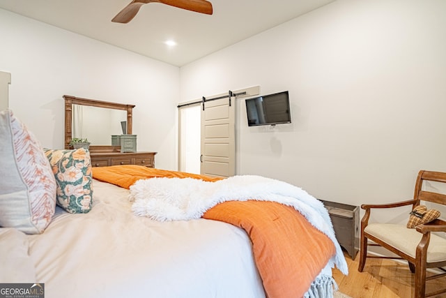 bedroom featuring wood-type flooring, a barn door, and ceiling fan