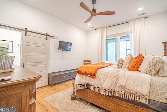 bedroom featuring a barn door, ceiling fan, and light hardwood / wood-style flooring