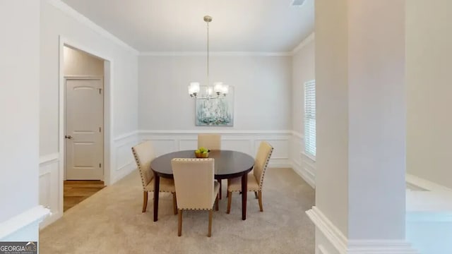 dining room with a wainscoted wall, ornamental molding, an inviting chandelier, and a decorative wall