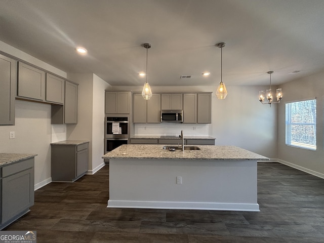 kitchen featuring light stone counters, gray cabinets, stainless steel appliances, and an island with sink