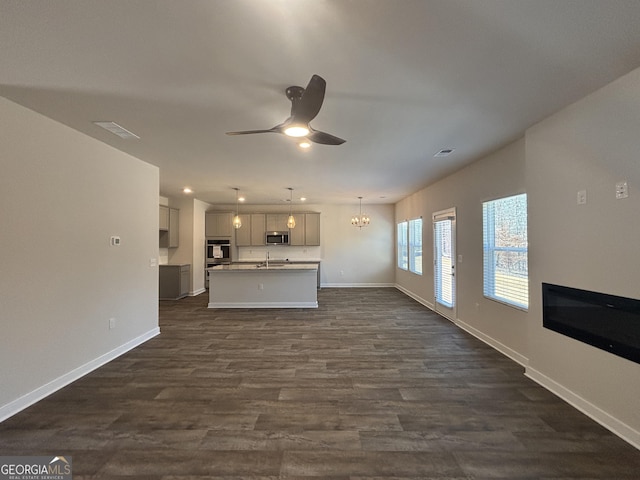 unfurnished living room featuring sink, ceiling fan with notable chandelier, and dark wood-type flooring