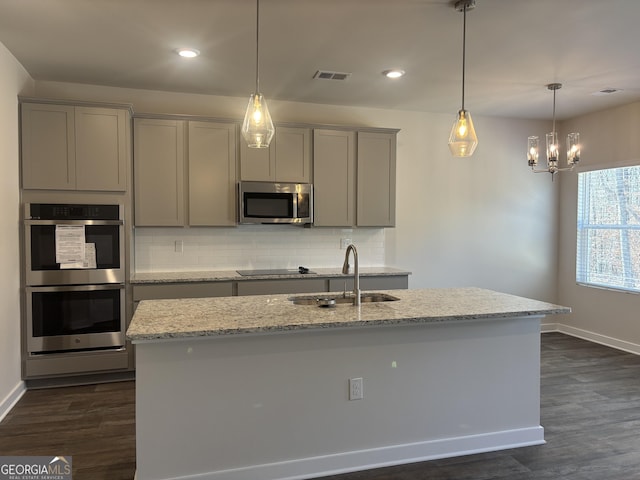 kitchen with light stone counters, appliances with stainless steel finishes, an island with sink, and gray cabinetry