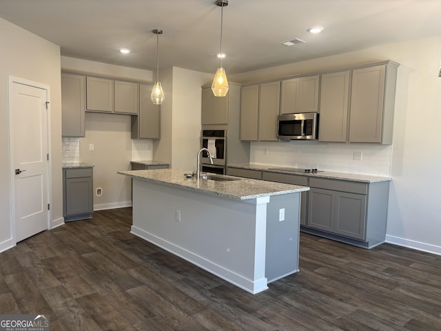 kitchen with light stone counters, gray cabinets, sink, and a center island with sink