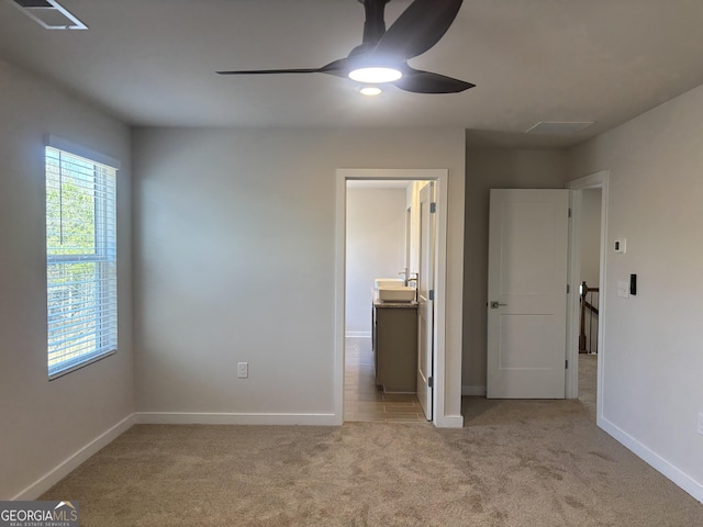 unfurnished bedroom with ceiling fan, light colored carpet, and ensuite bath