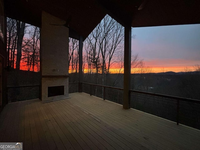 deck at dusk with a large fireplace and ceiling fan