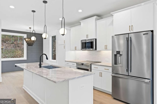 kitchen featuring decorative light fixtures, stainless steel appliances, light stone countertops, a kitchen island with sink, and white cabinets