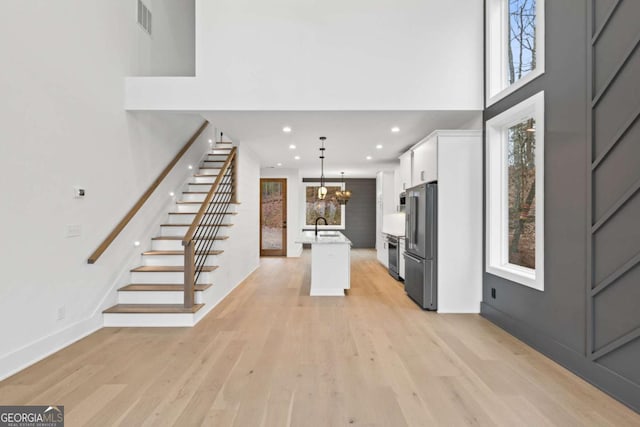 kitchen with white cabinetry, high end refrigerator, decorative light fixtures, a center island with sink, and light hardwood / wood-style flooring