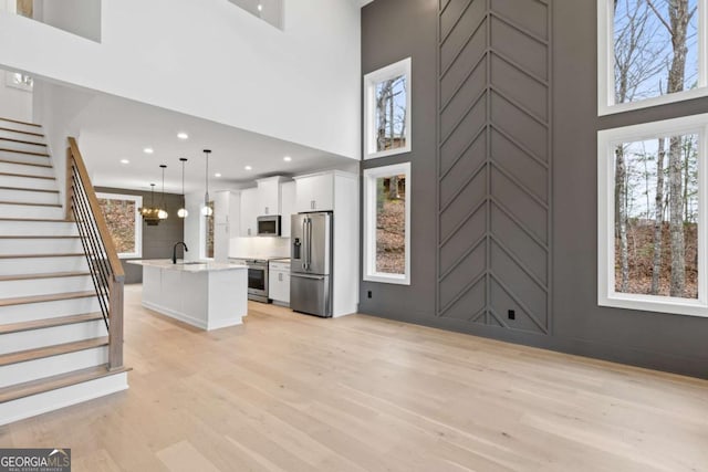 unfurnished living room with sink, a towering ceiling, a notable chandelier, and light wood-type flooring