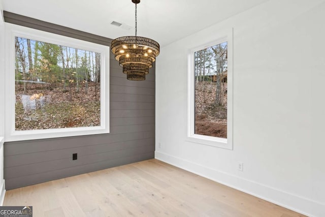 unfurnished dining area with light hardwood / wood-style flooring, a notable chandelier, a wealth of natural light, and wooden walls