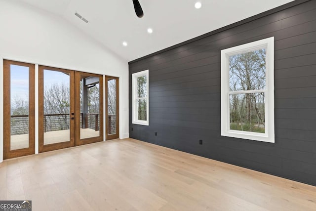 unfurnished room featuring french doors, high vaulted ceiling, light hardwood / wood-style flooring, and wood walls