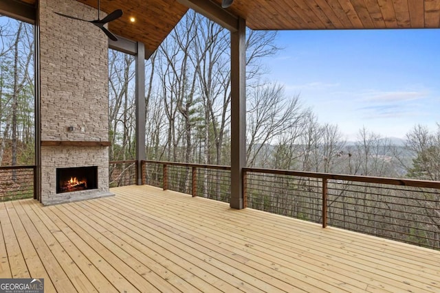 wooden deck featuring ceiling fan and an outdoor stone fireplace