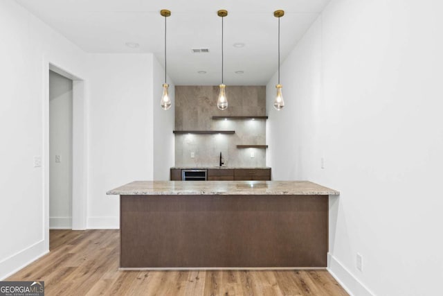 kitchen with light hardwood / wood-style flooring, pendant lighting, light stone counters, and kitchen peninsula