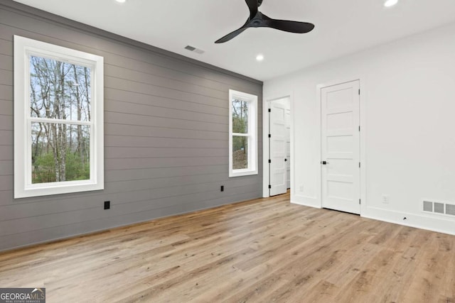 unfurnished bedroom featuring light hardwood / wood-style flooring, ceiling fan, and wood walls