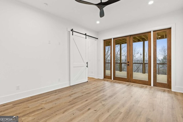 interior space with french doors, light hardwood / wood-style flooring, access to outside, ceiling fan, and a barn door