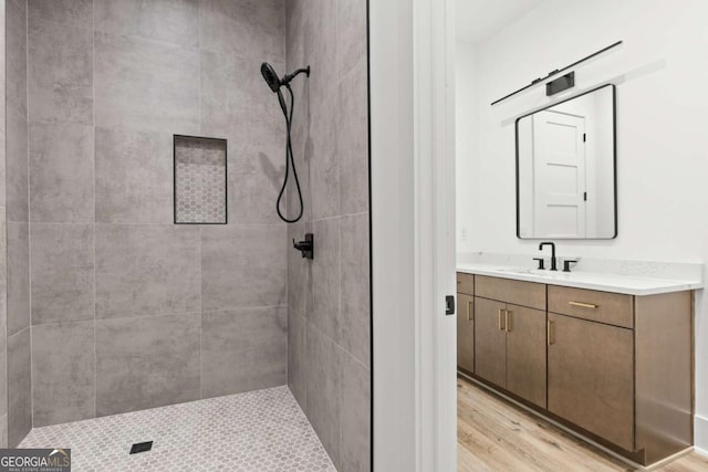 bathroom with hardwood / wood-style flooring, tiled shower, and vanity