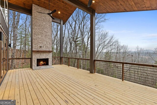 wooden deck featuring ceiling fan and an outdoor stone fireplace