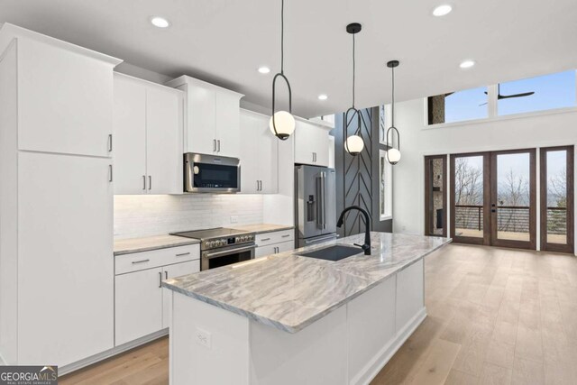 kitchen with sink, white cabinetry, decorative light fixtures, a center island with sink, and appliances with stainless steel finishes