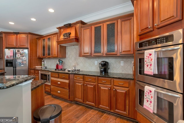 kitchen with appliances with stainless steel finishes, backsplash, ornamental molding, light hardwood / wood-style floors, and dark stone counters