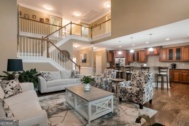 living room featuring hardwood / wood-style flooring, ornamental molding, sink, and a towering ceiling