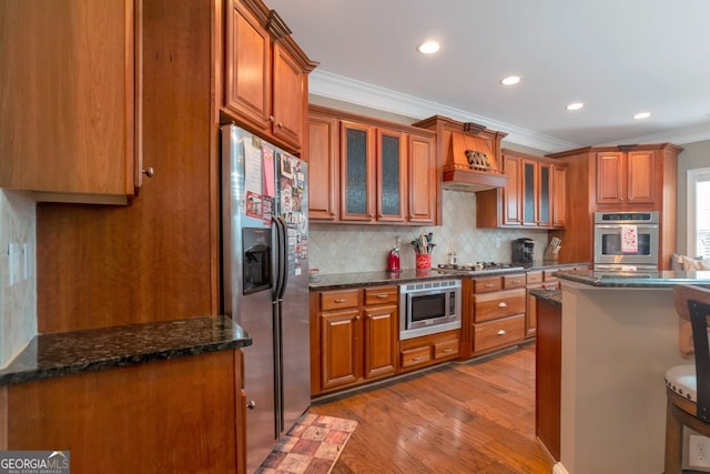 kitchen with crown molding, light wood-type flooring, appliances with stainless steel finishes, dark stone counters, and decorative backsplash