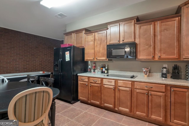 kitchen with light tile patterned flooring, brick wall, and black appliances