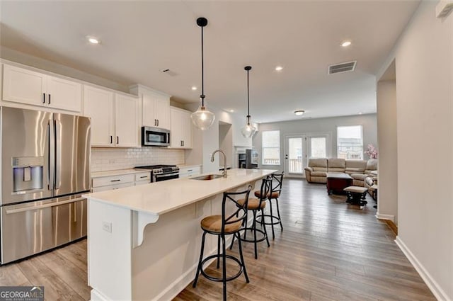 kitchen with sink, appliances with stainless steel finishes, white cabinetry, hanging light fixtures, and a center island with sink