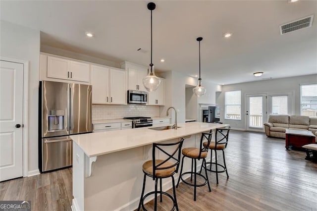 kitchen with sink, white cabinetry, appliances with stainless steel finishes, pendant lighting, and a kitchen island with sink