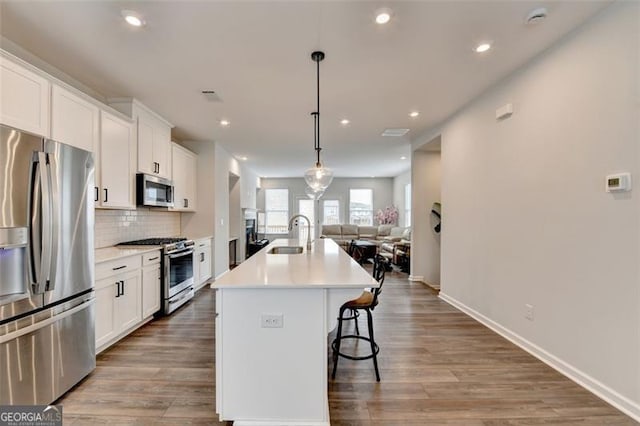 kitchen with stainless steel appliances, decorative light fixtures, an island with sink, and white cabinets