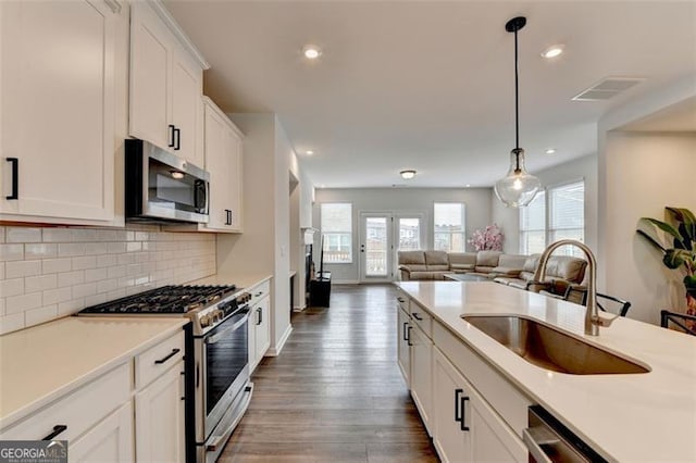 kitchen with sink, white cabinetry, hanging light fixtures, stainless steel appliances, and backsplash