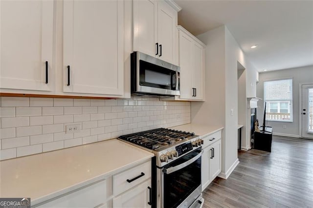 kitchen featuring wood-type flooring, appliances with stainless steel finishes, white cabinets, and decorative backsplash