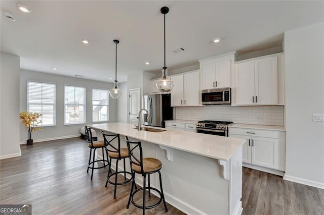 kitchen featuring stainless steel appliances, a center island with sink, white cabinets, and decorative light fixtures