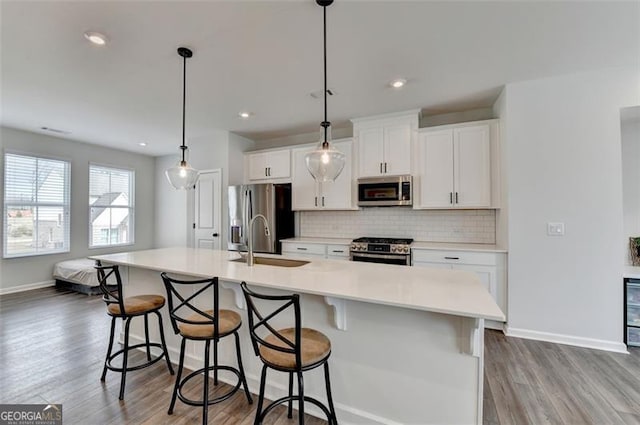 kitchen featuring white cabinetry, tasteful backsplash, a center island with sink, appliances with stainless steel finishes, and pendant lighting