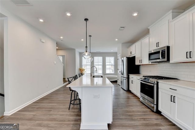 kitchen with a breakfast bar area, decorative light fixtures, appliances with stainless steel finishes, a kitchen island with sink, and white cabinets