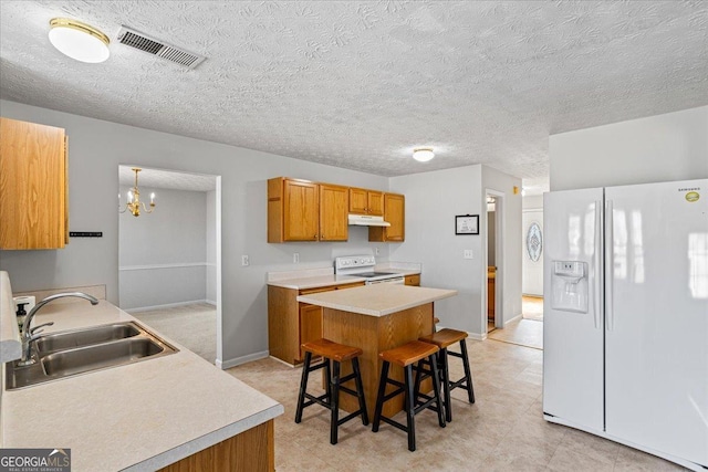 kitchen featuring a kitchen bar, sink, a textured ceiling, a kitchen island, and white appliances