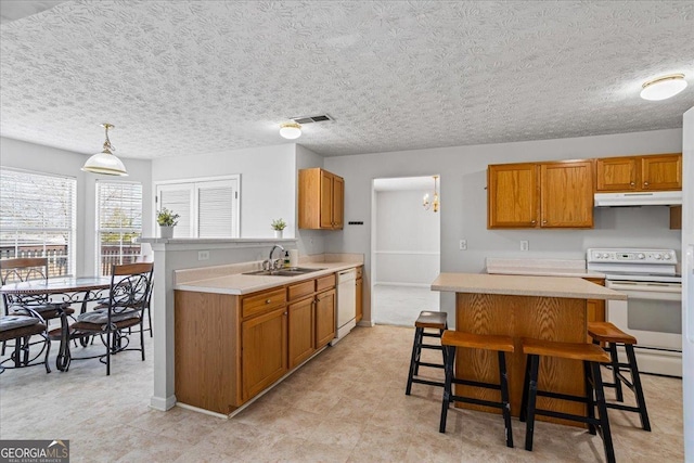 kitchen with a kitchen bar, sink, hanging light fixtures, a kitchen island, and white appliances