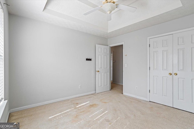 unfurnished bedroom with ceiling fan, a raised ceiling, a textured ceiling, light colored carpet, and a closet