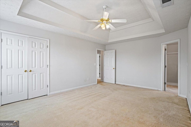 unfurnished bedroom featuring light carpet, a textured ceiling, a tray ceiling, a closet, and ceiling fan