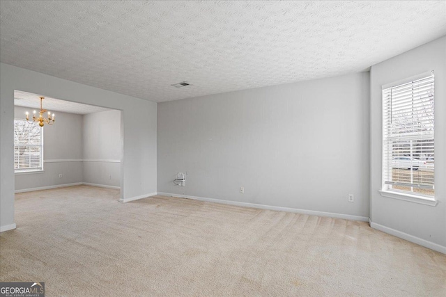 unfurnished room featuring an inviting chandelier, light carpet, and a textured ceiling